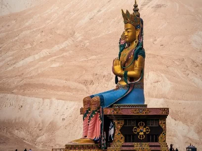 Towering Maitreya Buddha statue Diskit Gompa golden robes blue skirt intricate throne sand dunes backdrop near Hunder Nubra Valley Ladakh monastery landmark camel safari tour package Leh adventure.