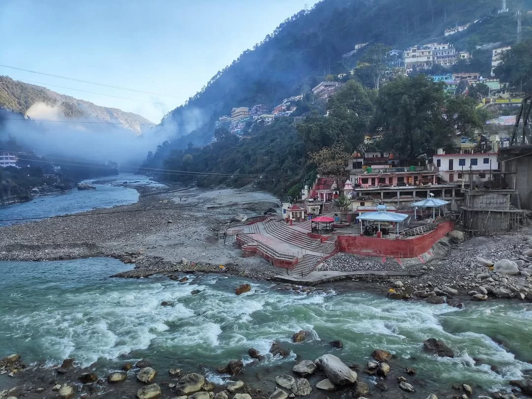 Red temple ghats at Karnaprayag during sunny morning mist, featuring turquoise river sandy banks pine mountains, perfect adventure experience Karnaprayag Uttarakhand Panch Prayag tour packages.