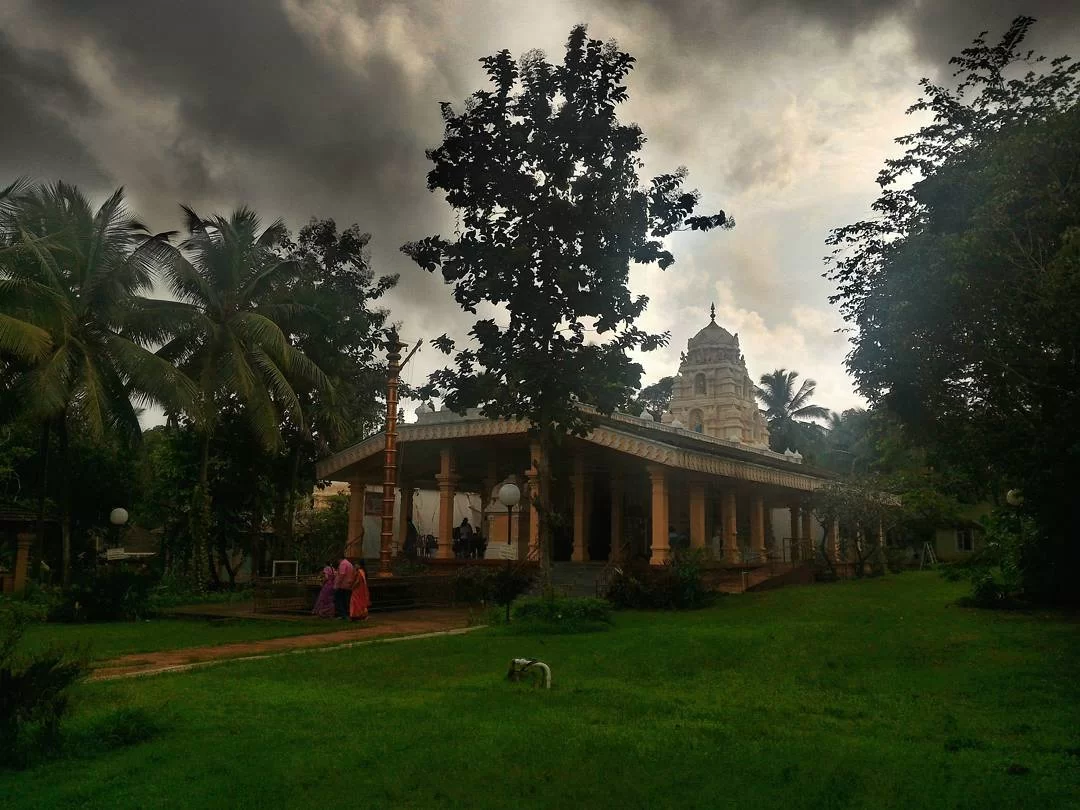 Traditional South Indian style Tirupati Balaji Temple in North Goa amid palm trees and cloudy skies, featuring devotees and serene temple pond, perfect spiritual visit with Goa tour package. 