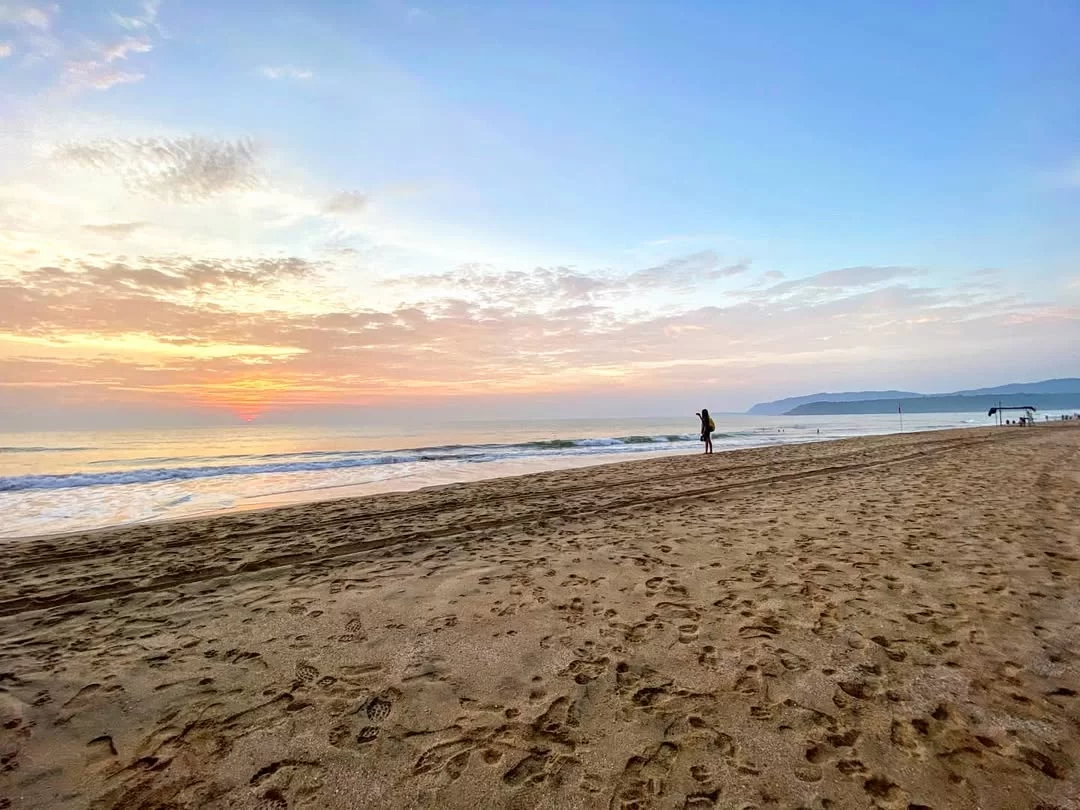 Silhouette at sunset on Agonda Beach Goa during dawn waves, featuring orange sky distant cliffs footprints sand, perfect romantic Goa tour package.