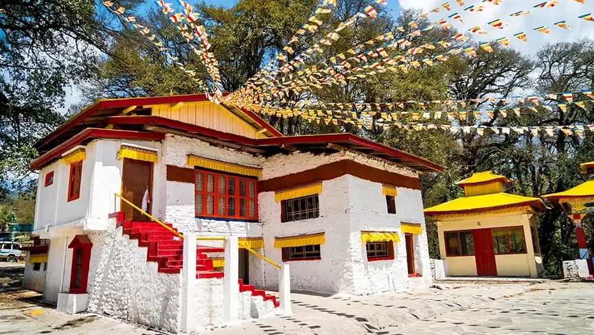 Ugyenling Monastery in Tawang featuring traditional white-washed architecture, colorful prayer flags, and peaceful forested surroundings, perfect spiritual experience with Tawang tour package.