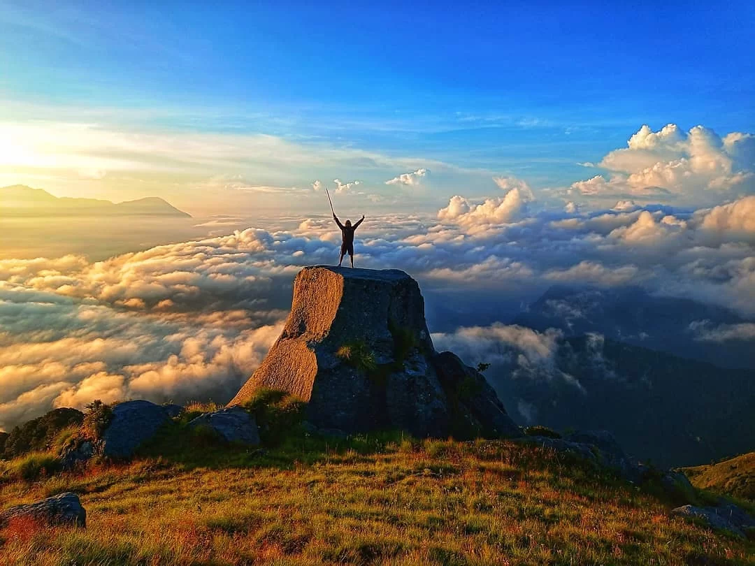 Adventurer celebrating sunset at Khaliya Top Munsiyari during golden hour, featuring rocky pinnacle, sea of clouds, mountains, perfect trekking adventure, Uttarakhand tour packages.