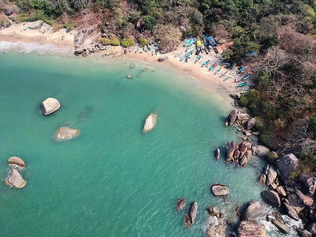 Kayaks on turquoise bay at Agonda Beach Goa during sunny day, featuring rocky outcrops sandy shore lush greenery, perfect romantic Goa tour package.
