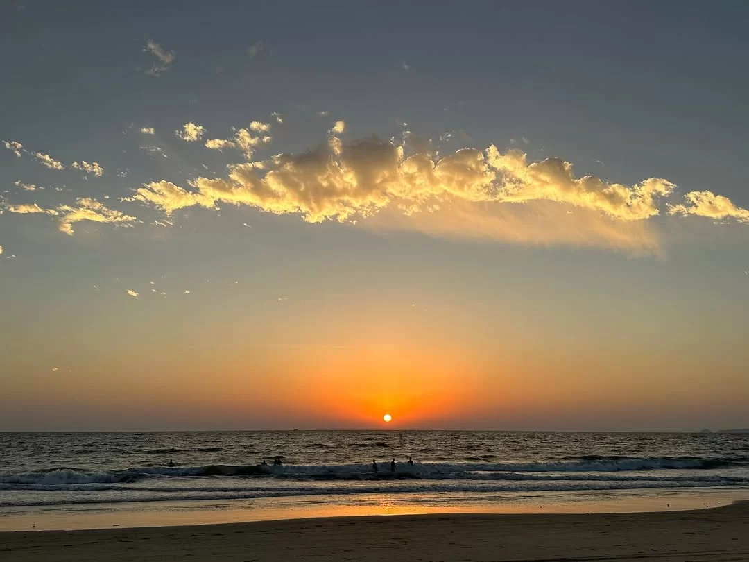 Vibrant sunset over Betalbatim Beach Goa golden hour, featuring glowing sun silhouetted clouds people swimming waves sandy shore, perfect South Goa beach tour package.