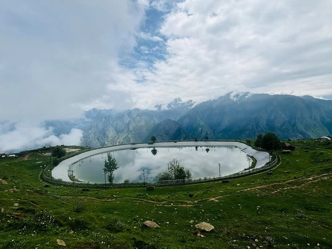Auli Artificial Lake Uttarakhand cloudy weather, featuring oval lake railing pine trees reflection misty snowcapped Himalayan peaks backdrop, perfect adventure experience Uttarakhand tour packages.
