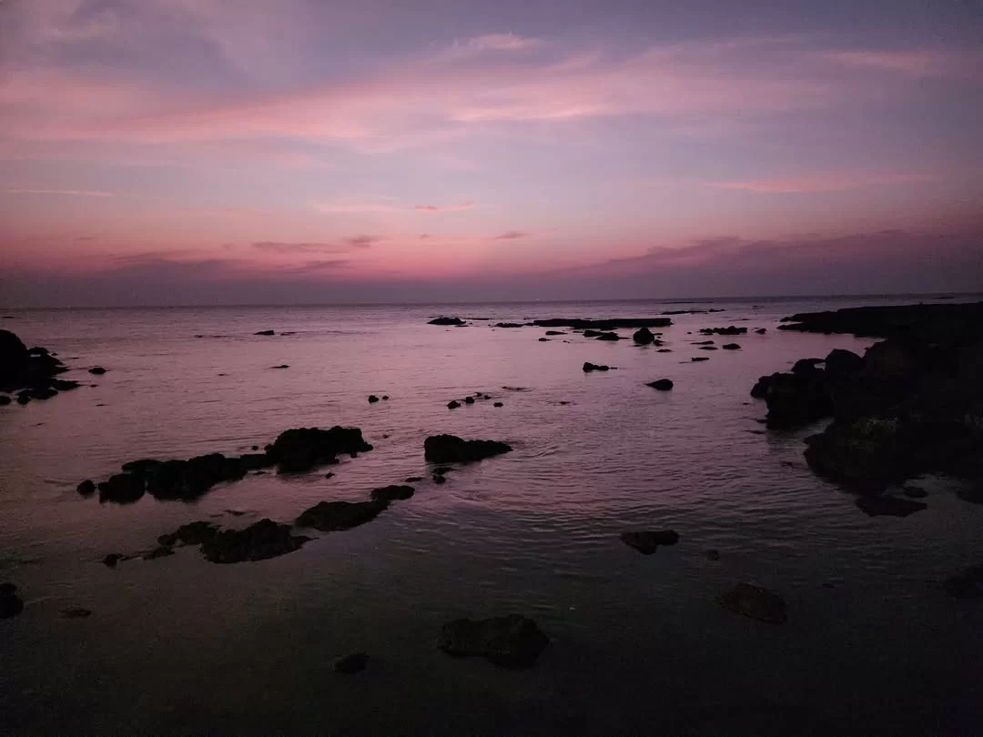 Purple sunset rocky coast at Dona Paula Beach Goa during twilight, featuring calm sea rocks distant horizon, perfect romantic experience Goa beach tour package.