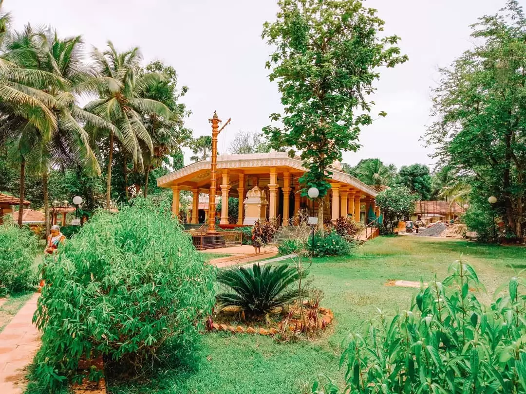 Serene Tirupati Balaji Temple North Goa surrounded by palm trees and greenery, featuring ornate pillars and lamp post, perfect peaceful spiritual retreat with Goa tour package. 