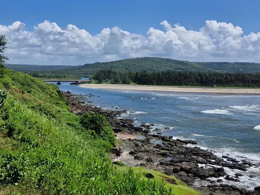 Aare Ware Beach in Maharashtra showcasing the scenic coastline with rocky shores, river estuary, green hills and clear blue sky, a peaceful destination often included in Maharashtra tour packages