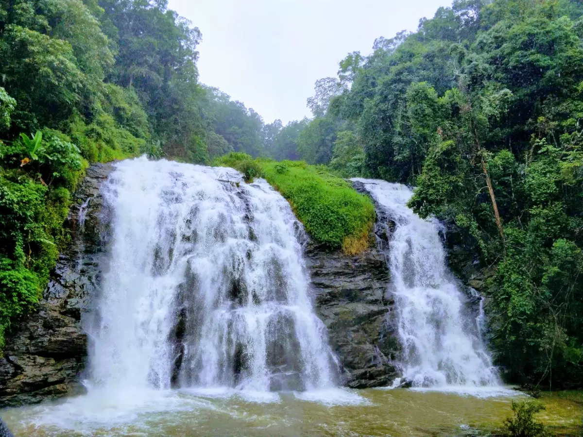 Abbey Falls at Coorg during cloudy day, featuring cascading waterfall, rocky tiers, forests, river pool, perfect nature experience Karnataka tour packages.