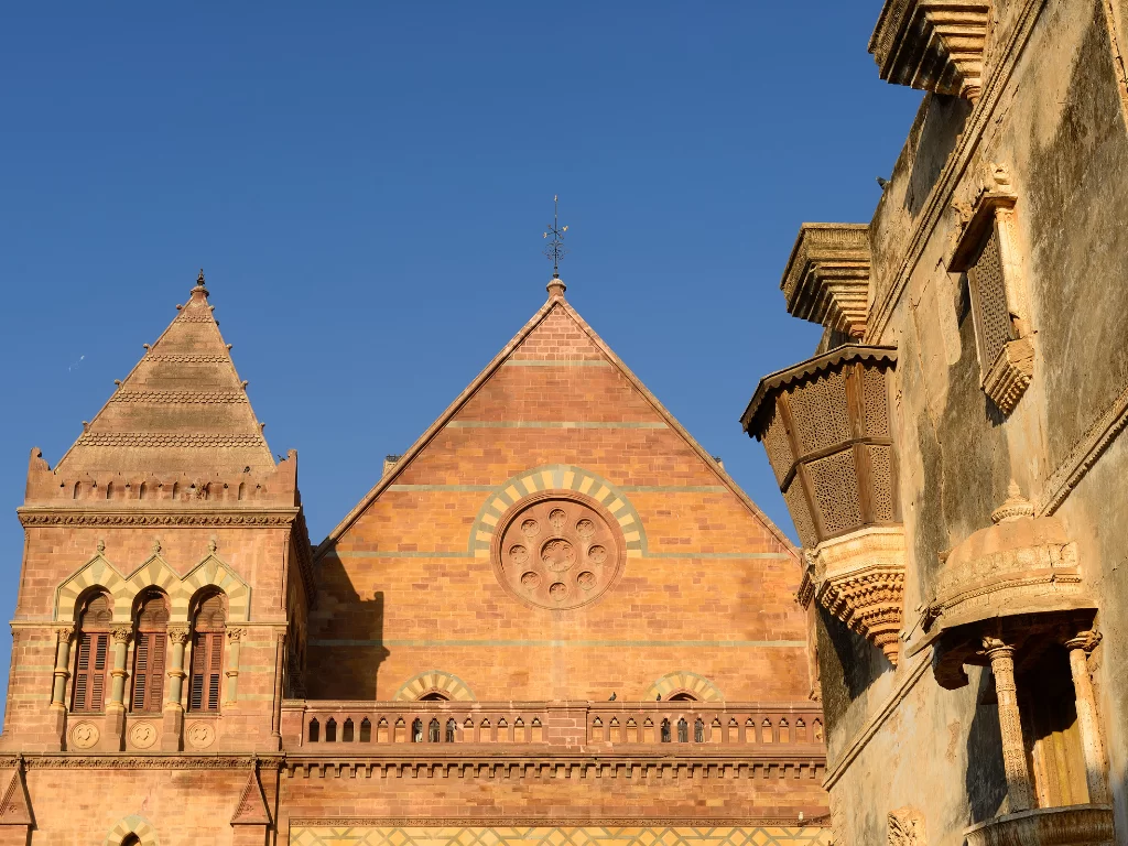 Aina Mahal palace facade in Bhuj, Kutch during golden hour, featuring Indo-European Gothic architecture with red sandstone gable roof, rose window, arched niches and adjacent traditional jharokhas, perfect heritage landmark with Gujarat tour packages.