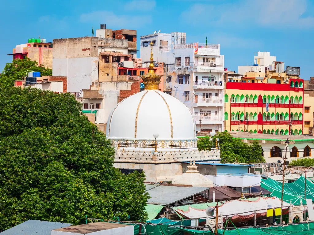 Ajmer Sharif Dargah white marble dome golden pinnacle Khwaja Moinuddin Chishti Sufi shrine surrounded by colorful urban buildings trees Rajasthan India historic mosque.
