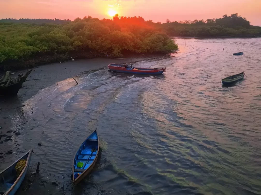 Sunset view at Akshi Beach in Alibaug, Maharashtra, with fishing boats resting near the mangrove-lined shore, a serene coastal escape included in Maharashtra tour packages.