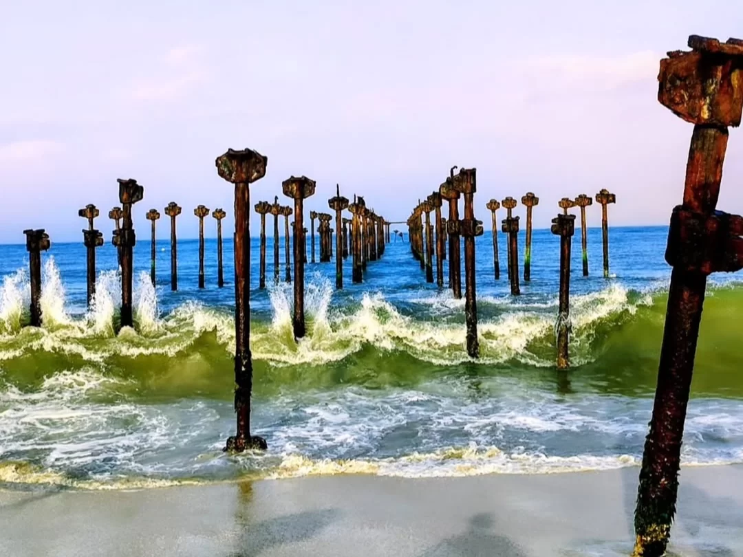 Alleppey Beach, Kerala India iconic old pier pillars in Arabian Sea with crashing waves and sandy shoreline.