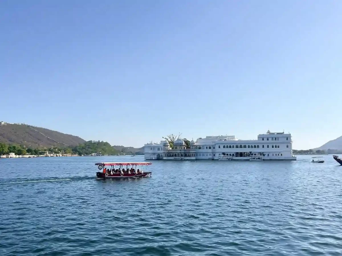 Ambrai Ghat view of Lake Pichola with a tourist boat and Taj Lake Palace, a top sightseeing spot in Udaipur.