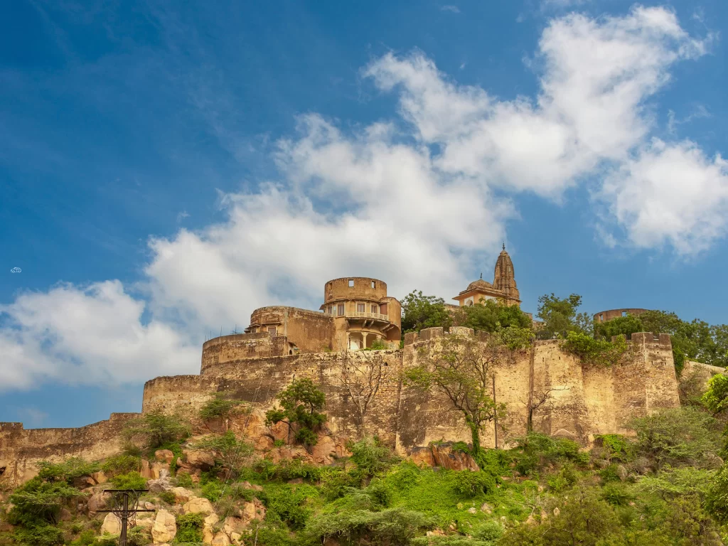 Wide angle view of Jaigarh Fort in Jaipur Rajasthan with bastioned walls, towers, greenery on hilltop under blue sky with scattered clouds, perfect Rajasthan tour package.