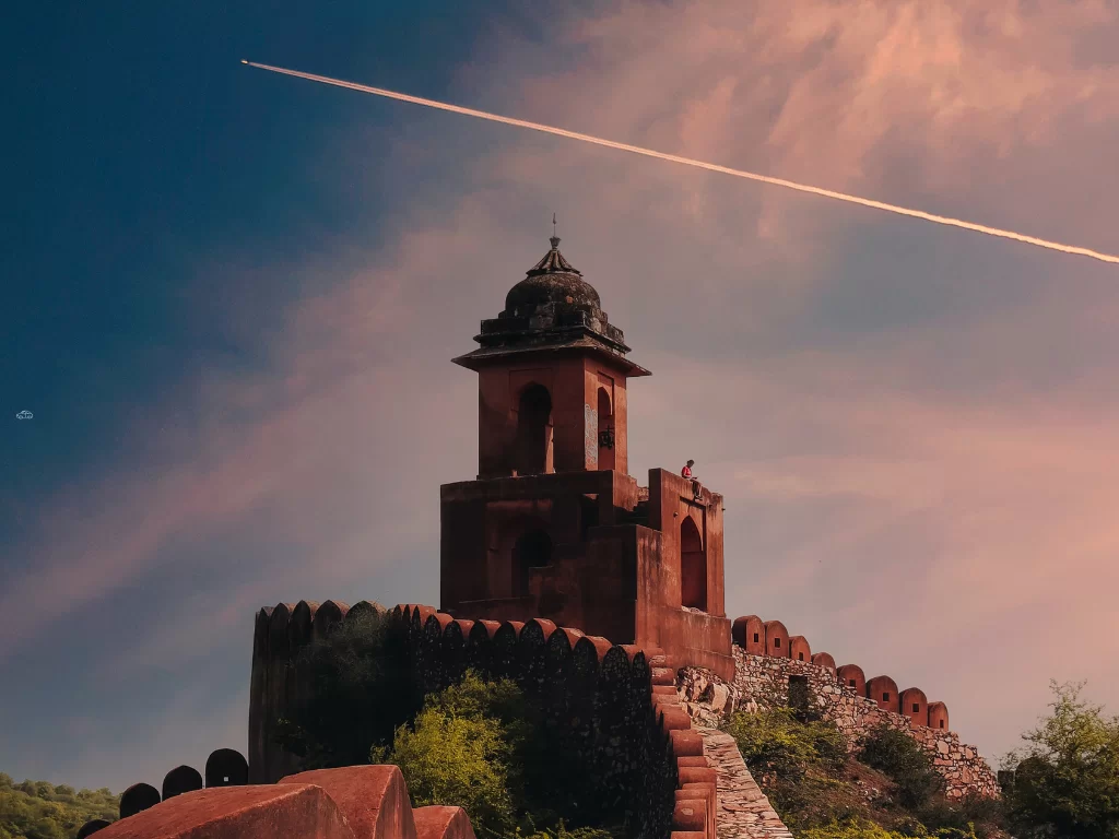 Watchtower on battlemented wall with dome pavilion at Jaigarh Fort in Jaipur Rajasthan amid greenery sunset pink sky airplane contrail background, perfect Rajasthan tour package.