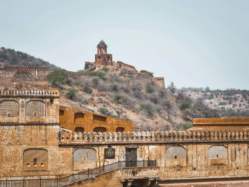 Ruined red sandstone structures with jharokhas railings staircase at Garh Ganesh Temple area near Jaigarh Fort in Jaipur Rajasthan hilltop watchtower background hazy blue sky, perfect Rajasthan tour package.