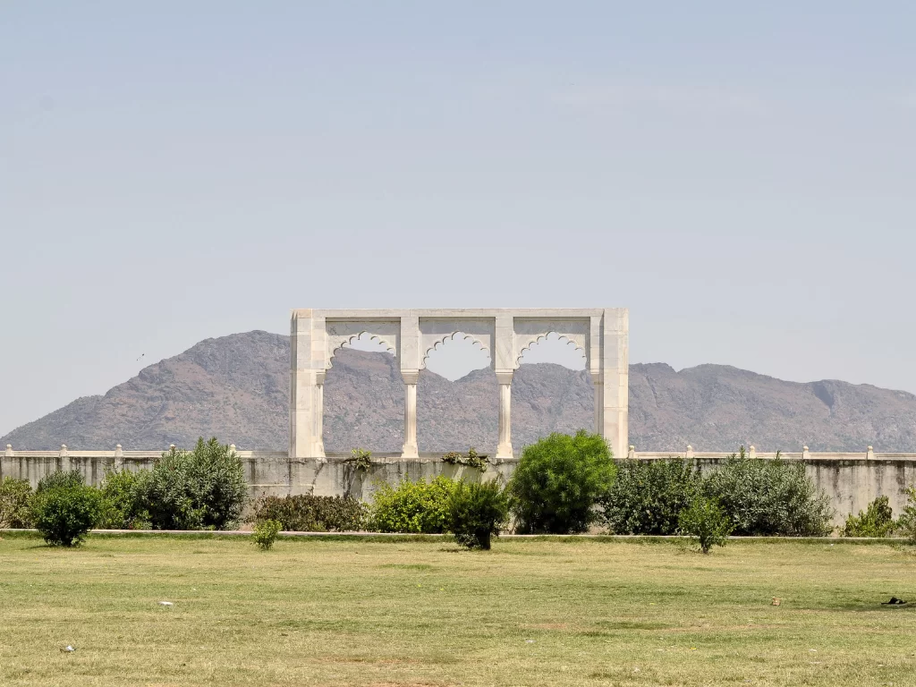 Baradari pavilion overlooking Ana Sagar Lake Ajmer Rajasthan with triple marble arches framing Aravalli hills lush gardens and hazy blue skies, classic heritage Rajasthan tour package landmark.