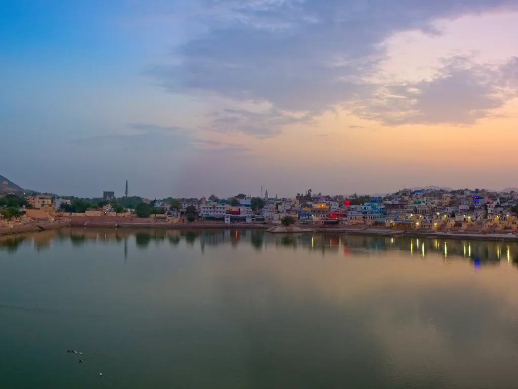 Ana Sagar Lake Ajmer Rajasthan at sunset with colorful skyline reflections lit ghats distant hills temple spires and twilight sky, stunning heritage Rajasthan tour package photography spot.