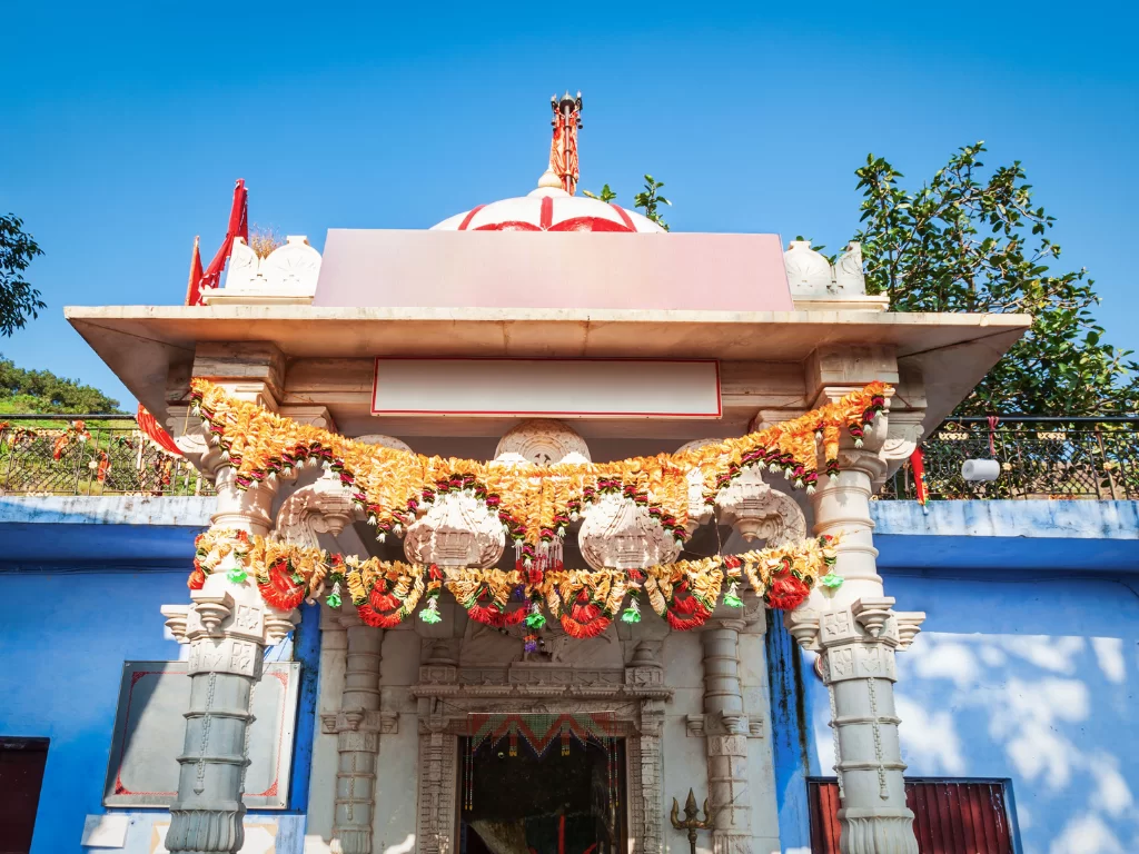 Arbuda Devi Temple ornate entrance garlands blue sky Mount Abu, white marble dome pillars orange marigold decorations trees hills, perfect Rajasthan tour packages.