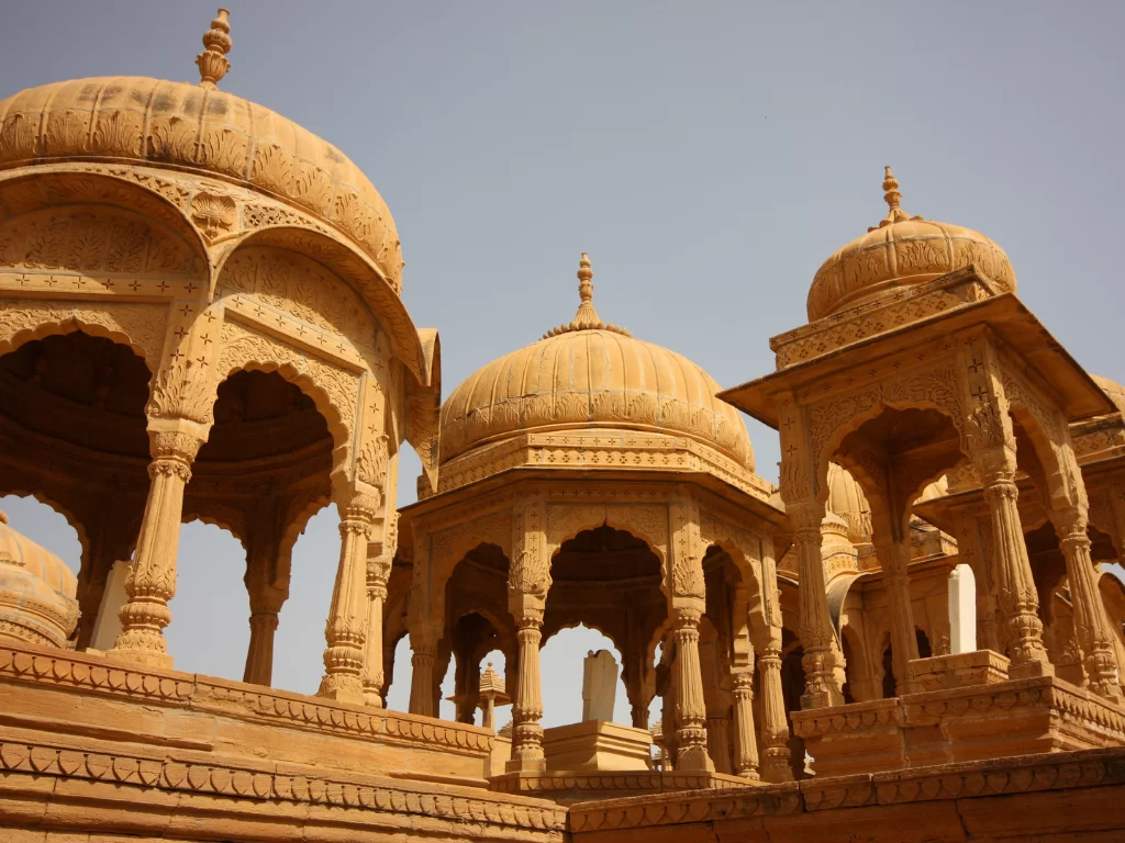 Bada Bagh Jaisalmer multiple golden sandstone chhatris domes arches pillars detailed carvings against hazy sky, perfect Rajasthan heritage cultural tour packages.