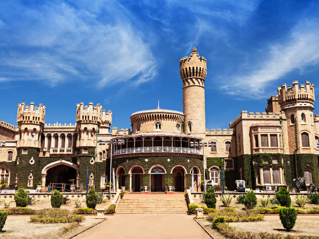 Bangalore Palace facade during sunny day, featuring Tudor towers, balconies, creepers, steps, gardens, perfect heritage experience Karnataka tour packages.
