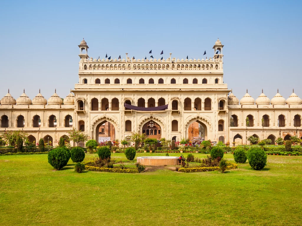 Bara Imambara at Lucknow during sunny day, featuring white facade domes arches gardens flags, perfect cultural Uttar Pradesh tour package.