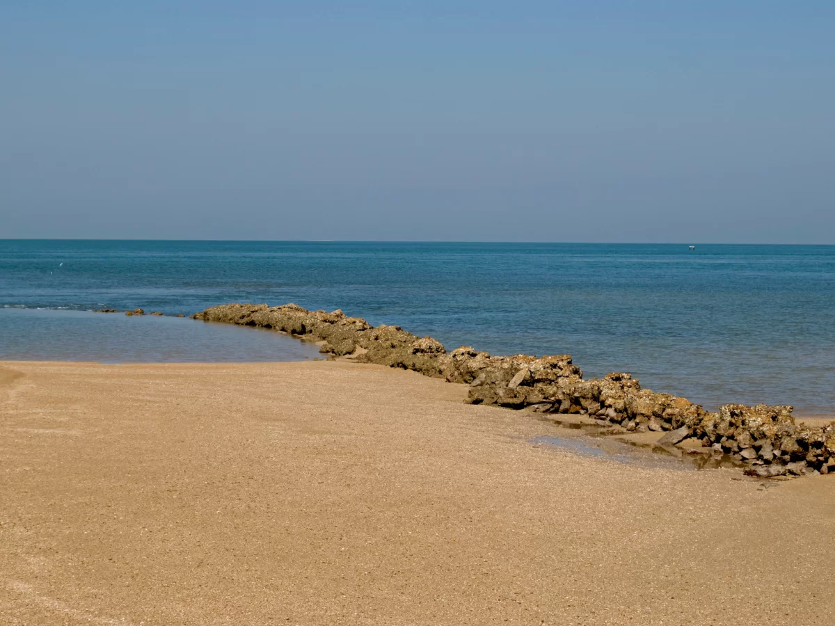 Beyt Dwarka beach during clear day, featuring sandy shore with rocky breakwater extending into turquoise Arabian Sea, perfect pilgrimage experience with Gujarat tour packages.