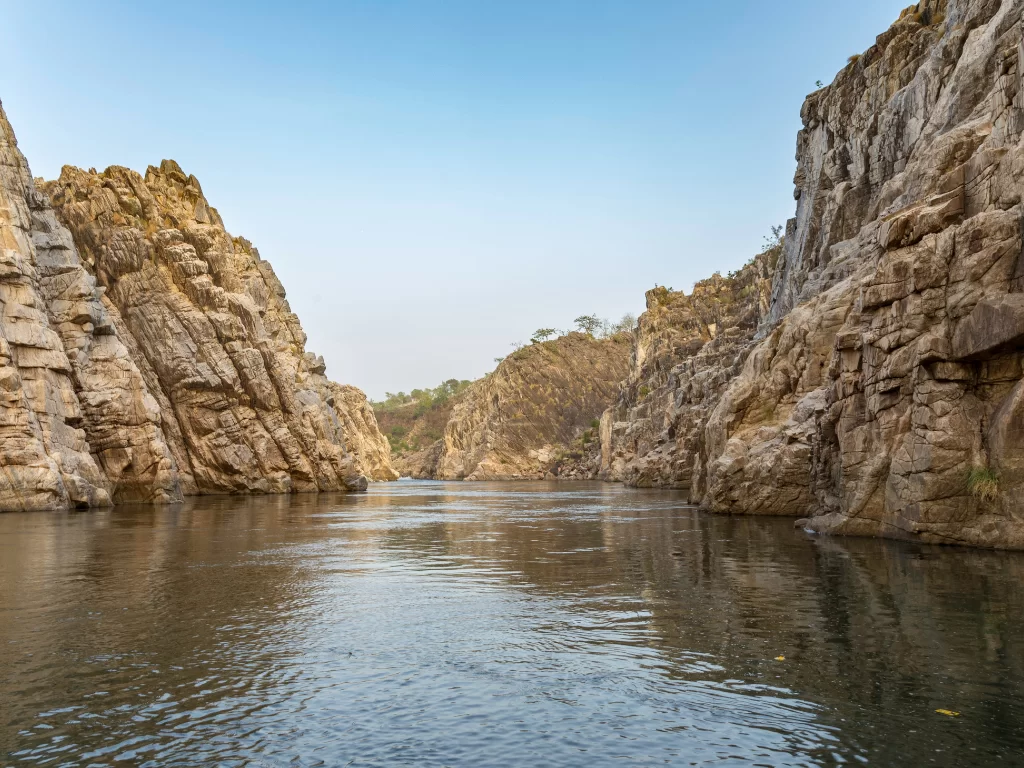 Marble Rocks canyon at Bhedaghat Jabalpur during clear afternoon, featuring towering white cliffs and serene Narmada River, perfect adventure experience in Madhya Pradesh tour package.
