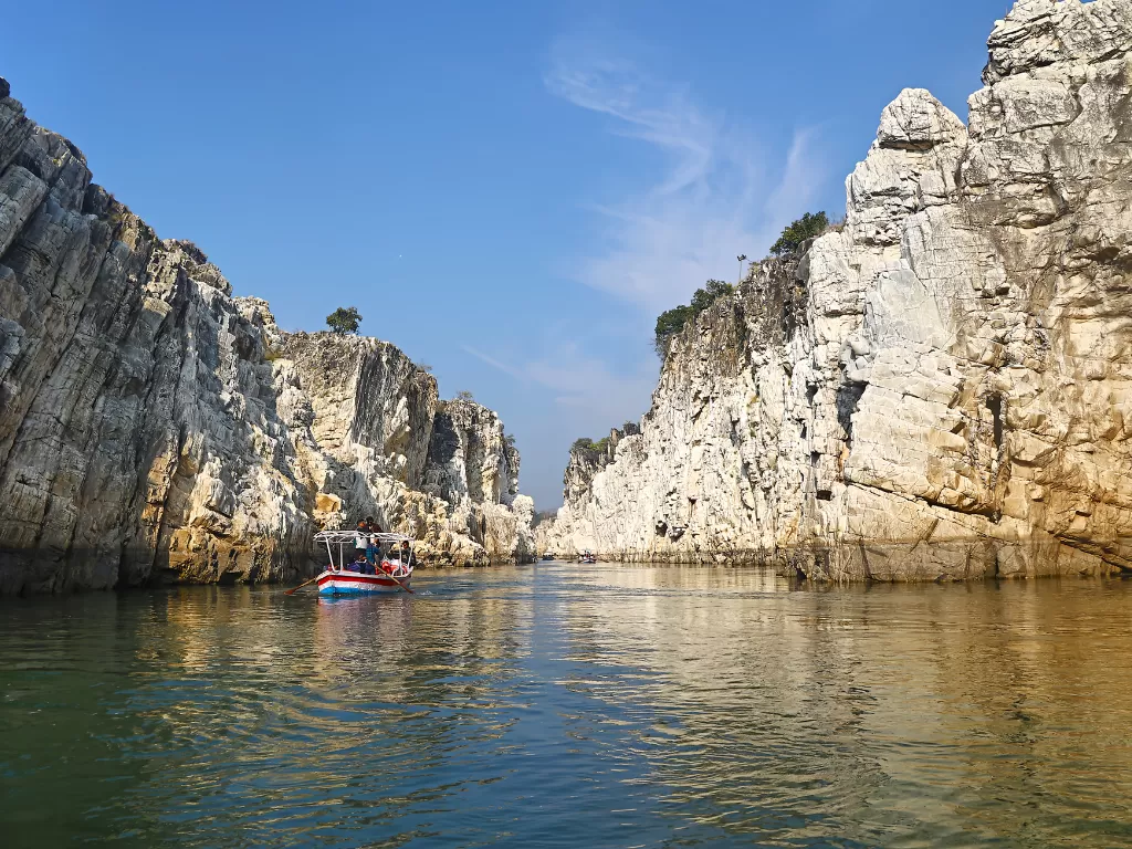 Boat ride through Marble Rocks at Bhedaghat Jabalpur during clear afternoon, featuring towering white cliffs and Narmada River reflections, perfect adventure experience in Madhya Pradesh tour package.