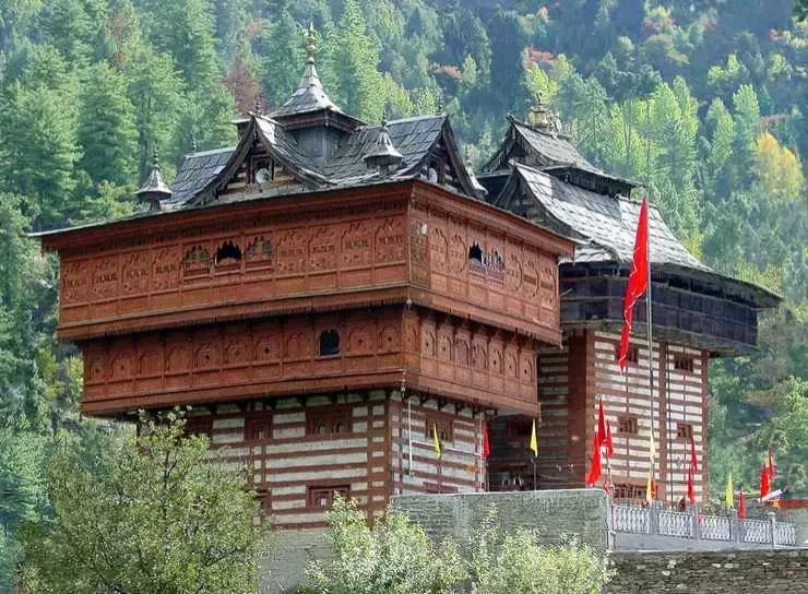 Shangchul Mahadev Temple at Shangarh Meadows Sainj Valley during autumn foliage, featuring carved wooden multi-story tower red flags pine forests mountains, perfect spiritual adventure Himachal Pradesh tour package.