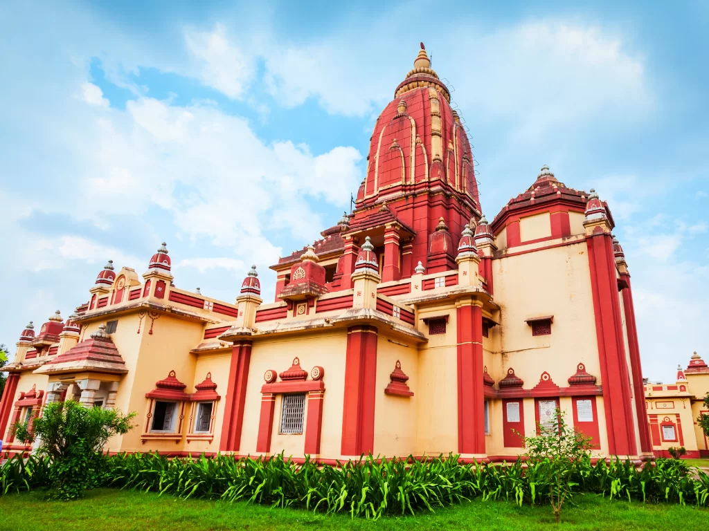 Mathura Birla Mandir Uttar Pradesh Gita Temple red sandstone architecture with golden spires, cream walls, intricate arches, lush green gardens under partly cloudy blue skies, perfect Krishna heritage India tour package.