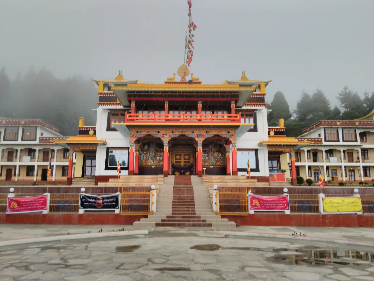Grand Thubten Gatsel Gompa at Bomdila Monastery during misty day, featuring prayer flags colorful facade hills forests, perfect spiritual experience Arunachal Pradesh tour package.