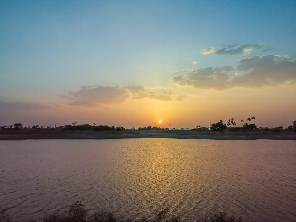 Bortalav Lake (Gaurishankar Lake) in Bhavnagar, Gujarat during sunset, featuring serene water reflections, silhouetted palm trees and colorful sky gradients, perfect natural landmark with Gujarat tour packages.