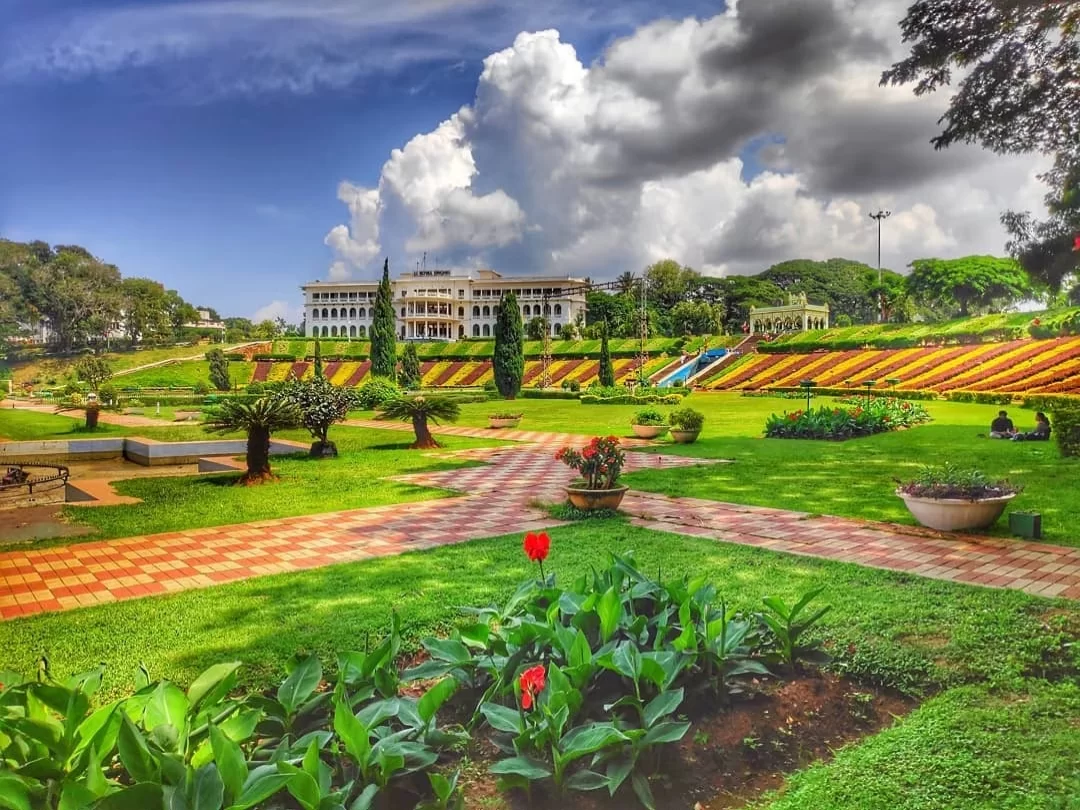 Brindavan Gardens at Mysore during cloudy day, featuring white palace terrace gardens lawns flowers cypress trees banyan palms, perfect garden experience Mysore tour package.