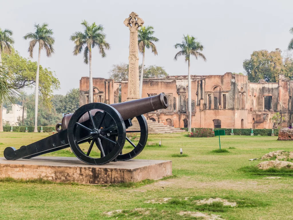 British Residency cannon cross at Lucknow during hazy day, featuring ruins palms lawns trees, perfect heritage Uttar Pradesh tour package.
