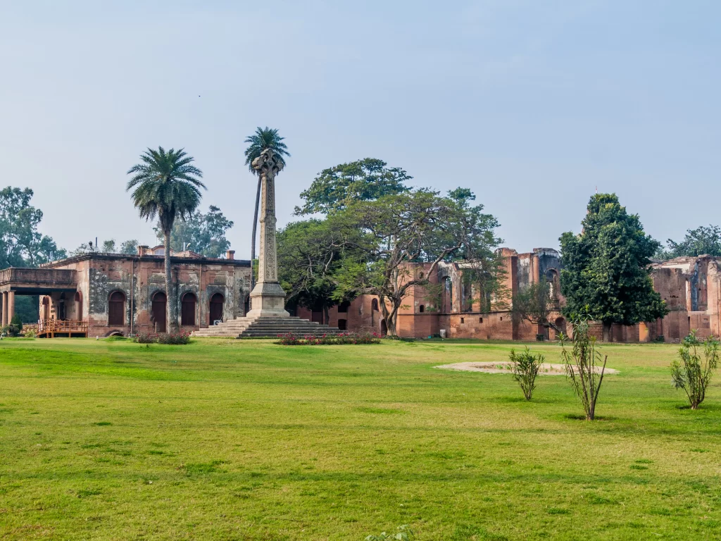 British Residency pillar ruins at Lucknow during clear day, featuring red brick arches palms trees lawns, perfect heritage Uttar Pradesh tour package.