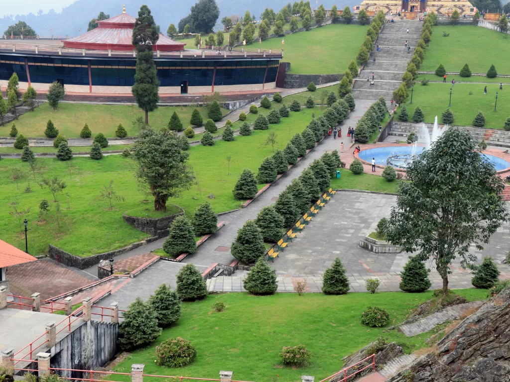 Terraced lawns and fountain at Buddha Park of Ravangla during cloudy daylight, featuring manicured pathways and rows of conifer trees, perfect spiritual Sikkim tour package.
