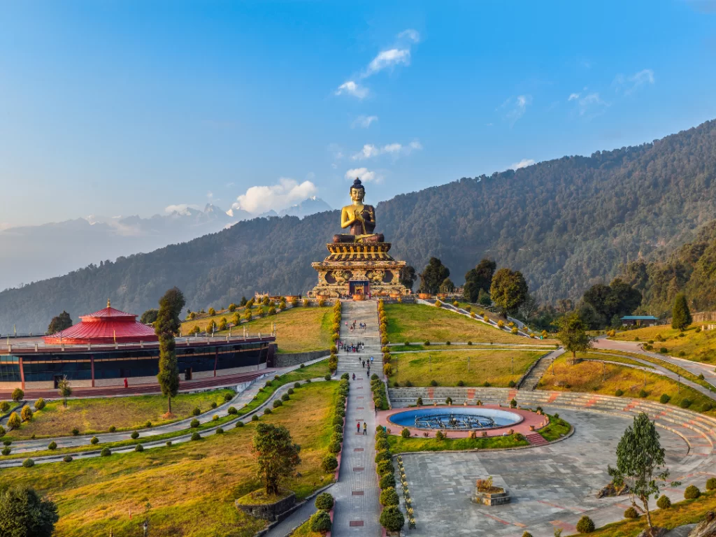 Panoramic view of Buddha Park of Ravangla during clear daylight, featuring massive Buddha statue, circular fountain and surrounding forested hills, perfect spiritual Sikkim tour package.