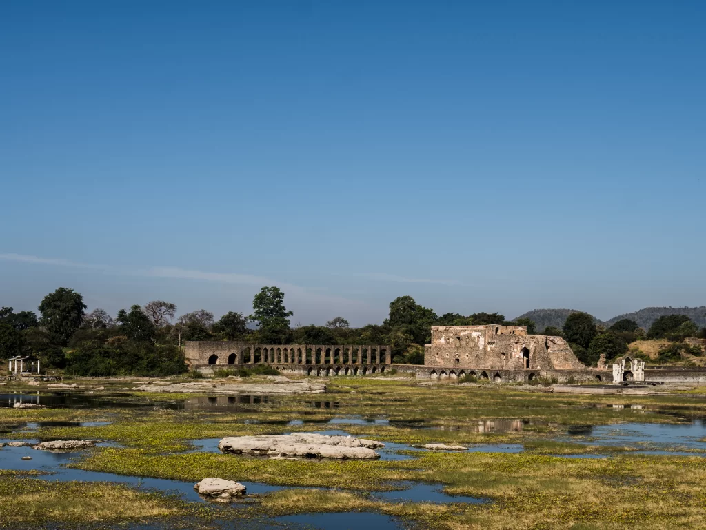 Rani Roopmati Pavilion at Mandu under clear skies, featuring Rewa Kund bridge ruins amid reservoir reflections, perfect heritage experience with Madhya Pradesh tour packages.