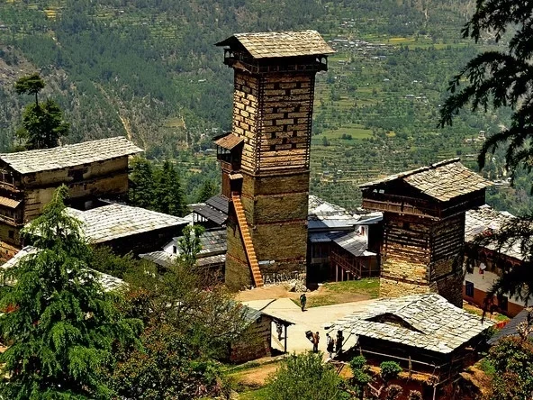 Chehni Kothi in Jibhi featuring a tall traditional Kath-Kuni style stone and wood tower surrounded by slate-roofed village houses and lush green mountain valley views.