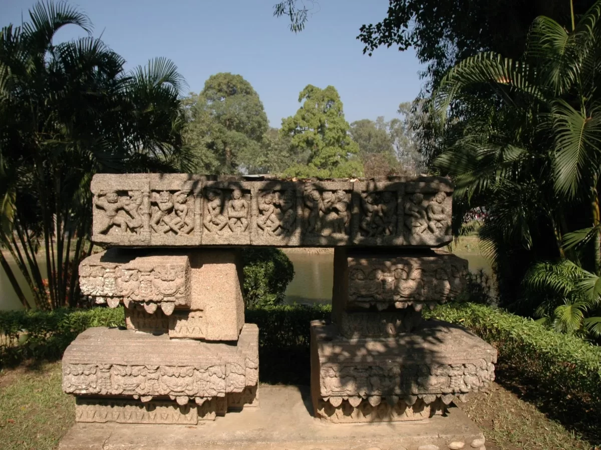 Chitralekha Udyan Tezpur ancient stone doorframe Bamuni Hills ruins intricate carvings palm trees blue sky pond background garden greenery, perfect historical landmark Tezpur Assam tour package.