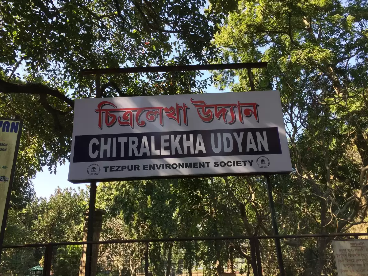 Chitralekha Udyan Tezpur entrance signboard bilingual Assamese English red white text Tezpur Environment Society trees blue sky fence, perfect historical park Tezpur Assam tour package.