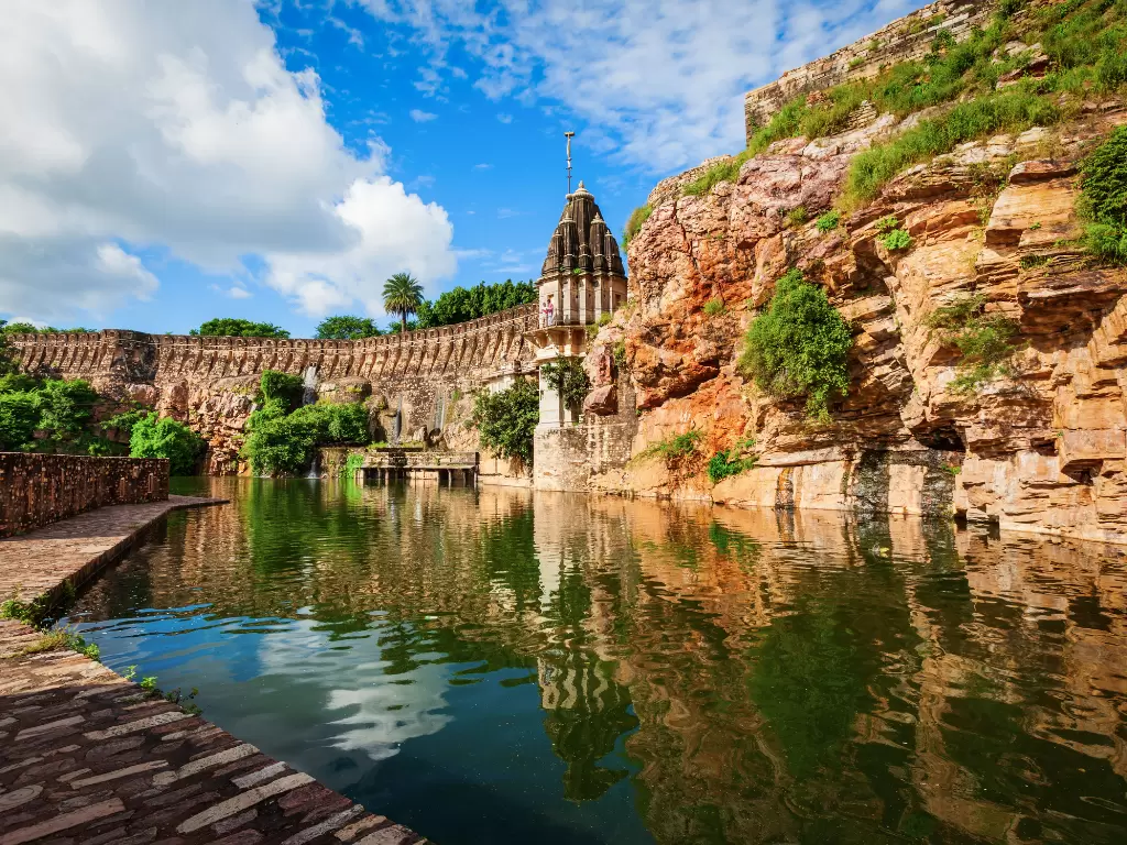Ancient walls and Vijay Stambh at Chittorgarh Fort in Rajasthan during sunny day, featuring cliffside temples and reservoir, perfect Rajasthan tour package.