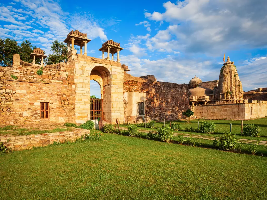Temple complex at Chittorgarh Fort in Rajasthan during golden hour, featuring stone gateway, lawns and shrines, perfect Rajasthan tour package.