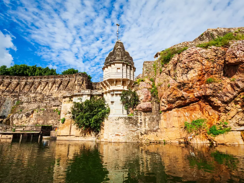 Temple by the lake at Chittorgarh Fort in Rajasthan under blue sky, featuring cliffs and water reflections, perfect Rajasthan tour package.