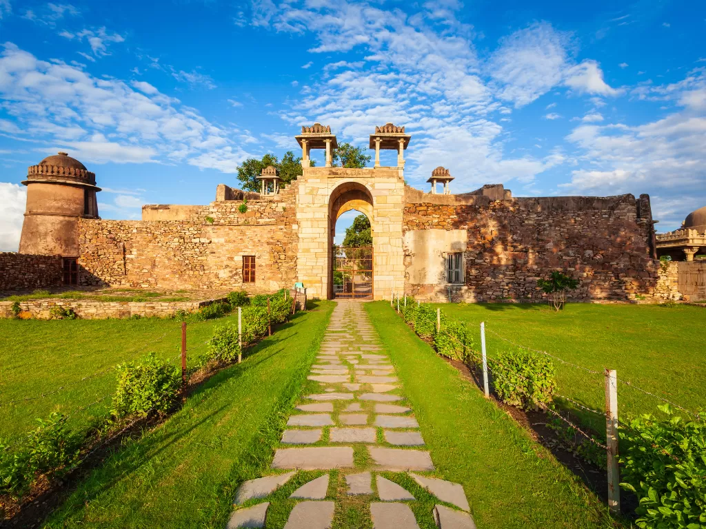 Stone gateway at Chittorgarh Fort in Rajasthan during golden hour, featuring green lawns and blue sky, perfect Rajasthan tour package.