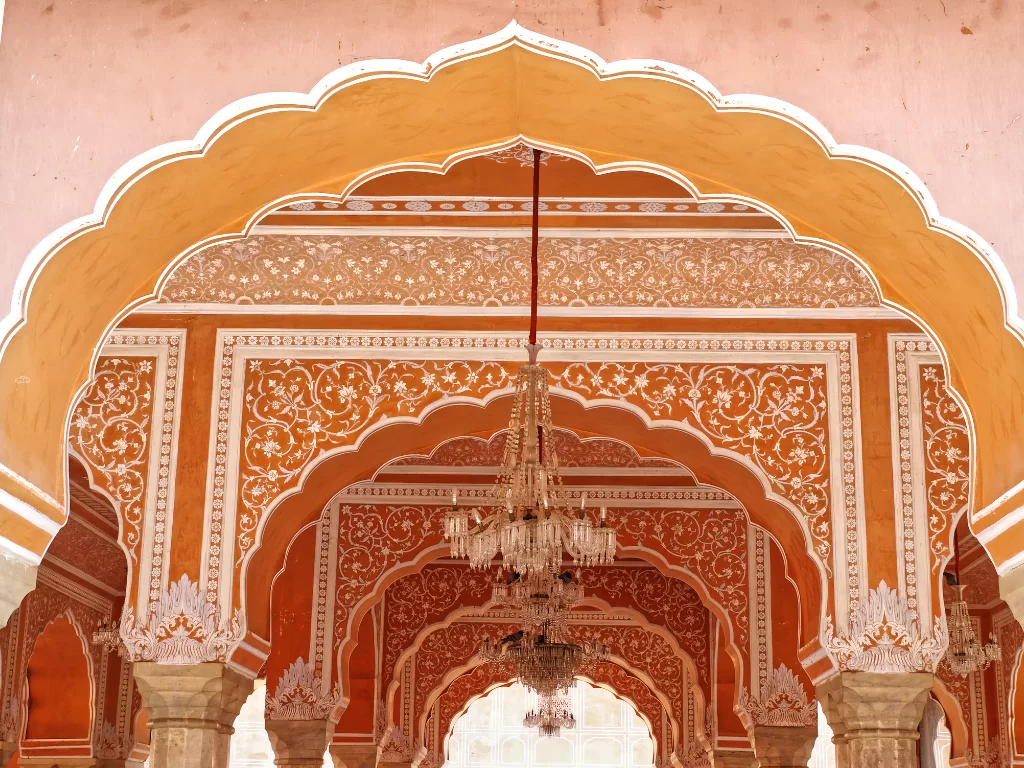 Ornate terracotta orange arched corridor with hanging chandeliers pillars intricate carvings City Palace Jaipur Rajasthan pink walls Rajput architecture, perfect Rajasthan tour package.