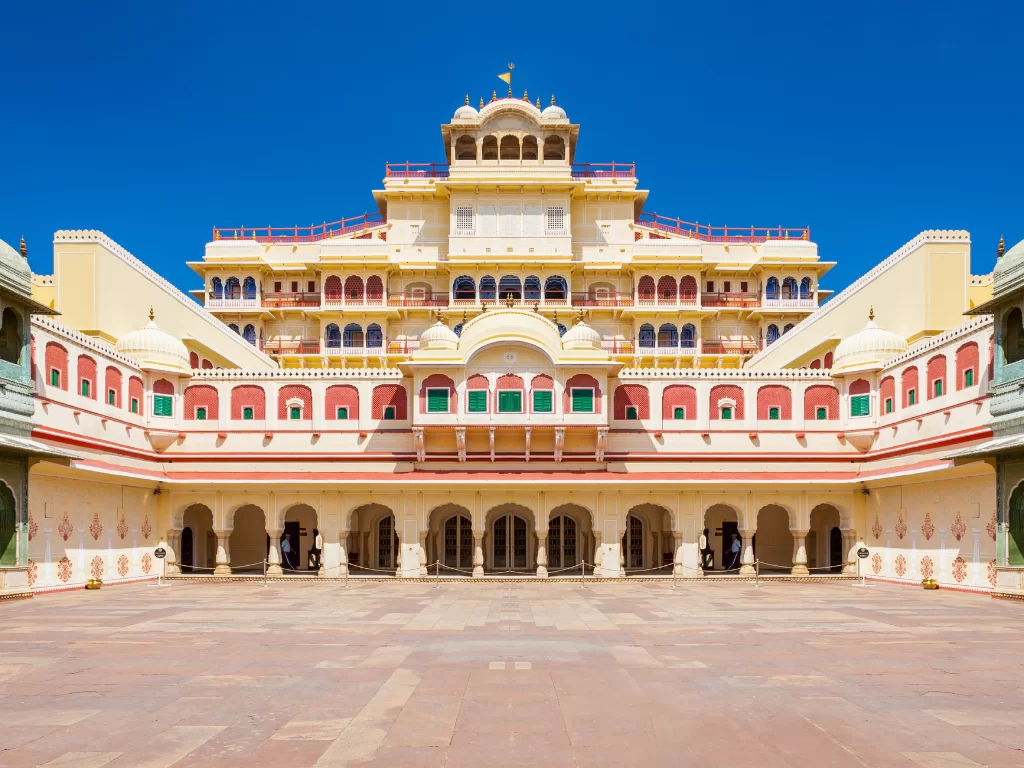 Iconic Chandra Mahal facade in central courtyard City Palace Jaipur Rajasthan with yellow towers pink arches green red wings open courtyard blue sky flags, perfect Rajasthan tour package