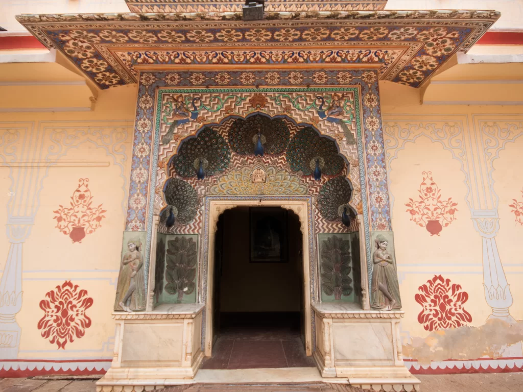 City Palace Jaipur Rajasthan magnificent peacock motif turquoise blue mosaic arched entranceway with detailed tilework gilded doors flanked by marble pillars pink walls floral accents, iconic Rajasthani royal palace gateway heritage tour package